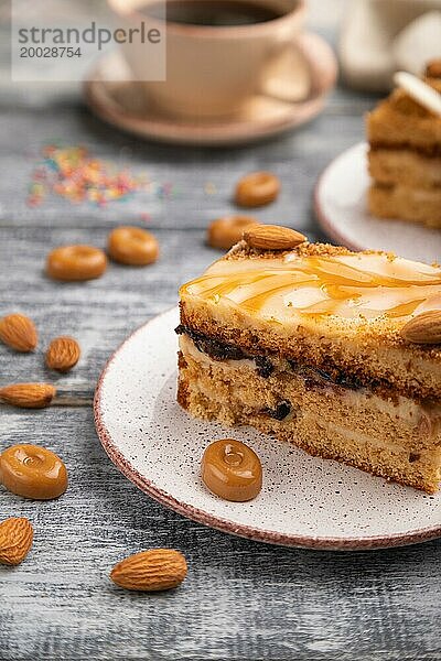 Honigkuchen mit Milchcreme  Karamell  Mandeln und einer Tasse Kaffee auf einem grauen Holzhintergrund und Leinenstoff. Seitenansicht  Nahaufnahme  selektiver Fokus