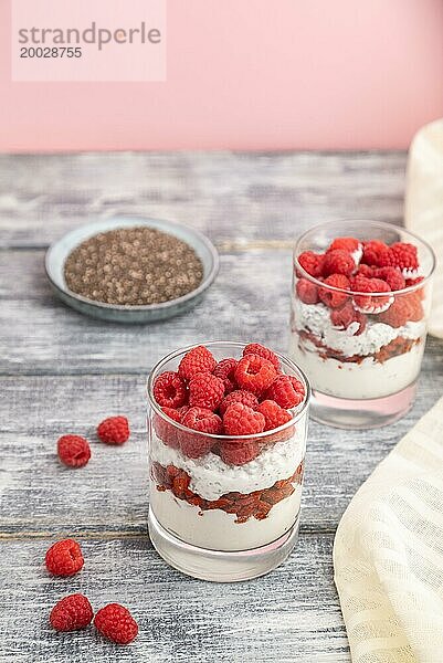 Joghurt mit Himbeeren  Goji Beeren und Chia Samen im Glas auf grauem Holzhintergrund und Leinenstoff. Seitenansicht  Nahaufnahme  selektiver Fokus