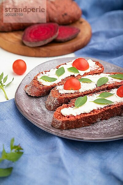 Rote Bete Brote mit Frischkäse und Tomaten auf weißem Betonhintergrund und blauem Leinentextil. Seitenansicht  selektiver Fokus  Nahaufnahme