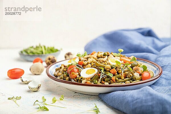 Mungobohnenbrei mit Wachteleiern  Tomaten und Mikrogrünsprossen auf einem weißen Betonhintergrund und blauem Textil. Seitenansicht  Kopierraum  selektiver Fokus