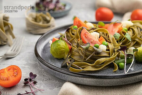 Tagliatelle mit grünem Spinat  Tomaten  Erbsen und Mikrosprossen auf grauem Betonhintergrund und Leinentuch. Seitenansicht  Nahaufnahme  selektiver Fokus