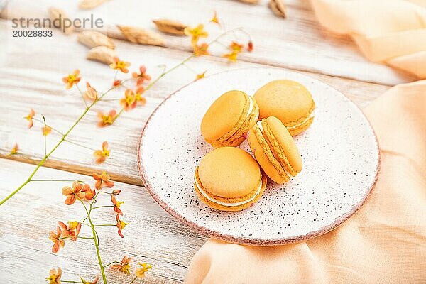 Orange Macarons oder Makronen Kuchen mit Tasse Aprikosensaft auf einem weißen hölzernen Hintergrund und orangefarbenen Leinen Textil. Seitenansicht  Nahaufnahme  selektiver Fokus