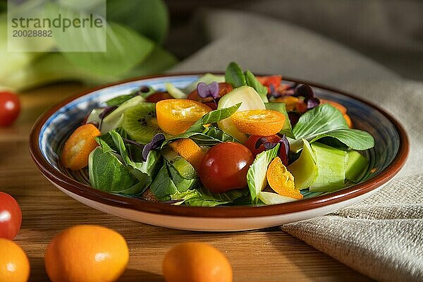 Vegetarischer Salat aus Pac Choi Kohl  Kiwi  Tomaten  Kumquat  mikrogrünen Sprossen auf einem hölzernen Hintergrund und Leinenstoff. Hartes Licht  Kontrast. Seitenansicht  Nahaufnahme  selektiver Fokus