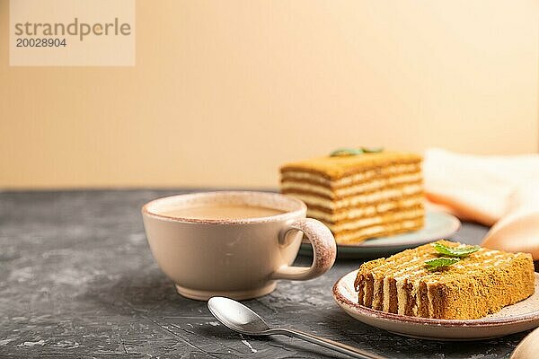 Hausgemachter Honigkuchen mit Milchcreme und Minze mit einer Tasse Kaffee auf einem schwarz orangenen Hintergrund und orangefarbenem Textil. Seitenansicht  Kopierraum  selektiver Fokus