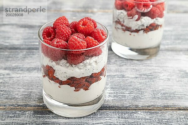 Joghurt mit Himbeeren  Goji Beeren und Chia Samen im Glas auf grauem Holzhintergrund. Seitenansicht  Nahaufnahme  selektiver Fokus