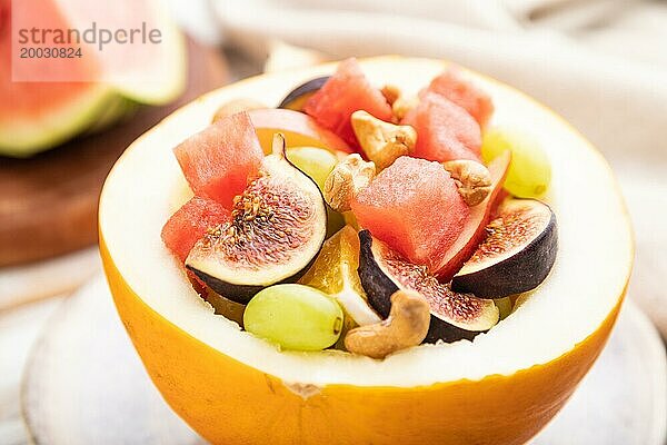 Vegetarischer Obstsalat aus Wassermelone  Trauben  Feigen  Birne  Orange  Cashew auf weißem Holzhintergrund und Leinentuch. Seitenansicht  Nahaufnahme  selektiver Fokus