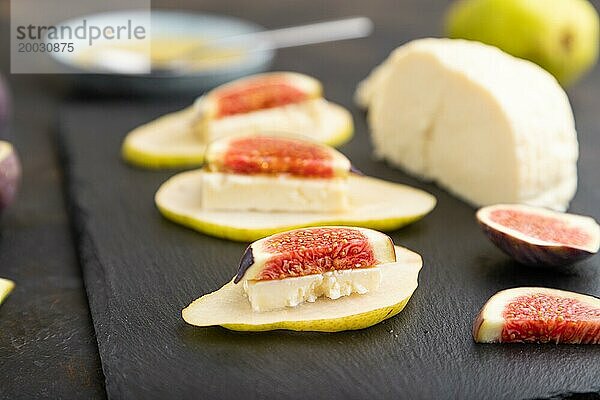 Sommerliche Vorspeise mit Birne  Hüttenkäse  Feigen und Honig auf Schieferplatte auf schwarzem Betonhintergrund. Seitenansicht  Nahaufnahme  selektiver Fokus