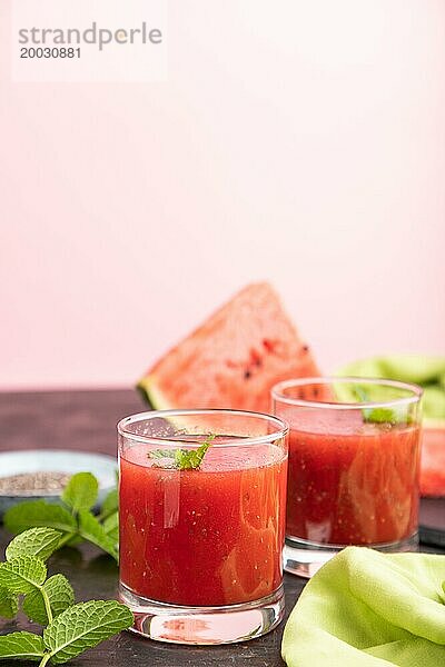 Wassermelonensaft mit Chiasamen und Minze in einem Glas auf einem schwarzen und rosa Hintergrund mit grünem Stoff. Gesundes Getränk Konzept. Seitenansicht  Nahaufnahme  selektiver Fokus  Kopierraum