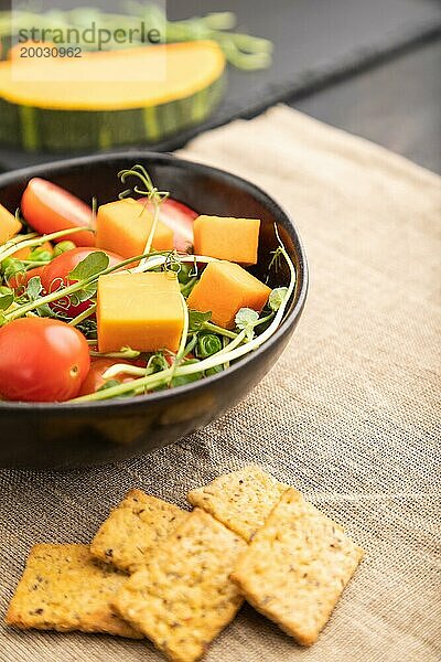 Vegetarischer Gemüsesalat aus Tomaten  Kürbis  mikrogrünen Erbsensprossen auf schwarzem Betonhintergrund und Leinentuch. Seitenansicht  Nahaufnahme  selektiver Fokus