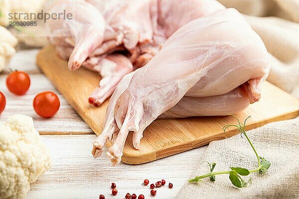 Ganzes rohes Kaninchen mit Blumenkohl  Tomaten und Gewürzen auf einem weißen Holzhintergrund und Leinenstoff. Seitenansicht  Nahaufnahme  selektiver Fokus