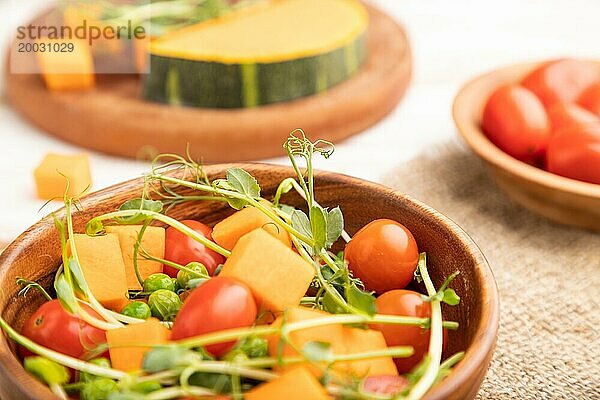 Vegetarischer Gemüsesalat aus Tomaten  Kürbis  mikrogrünen Erbsensprossen auf weißem Holzhintergrund und Leinentuch. Seitenansicht  Nahaufnahme  selektiver Fokus