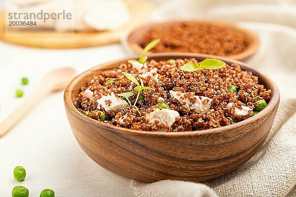 Quinoa Brei mit grünen Erbsen und Huhn in einer Holzschüssel auf einem weißen Holzhintergrund und Leinenstoff. Seitenansicht  Nahaufnahme  selektiver Fokus