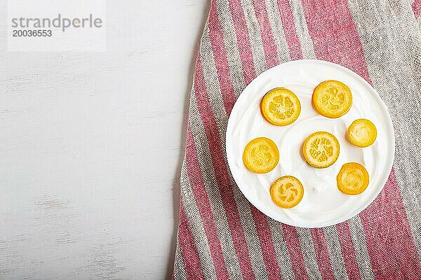 Griechischer Joghurt mit Kumquat Stücken in einem weißen Teller auf weißem Holzhintergrund  Draufsicht  Flat Lay  Copy Space