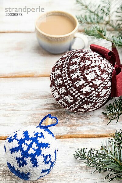 Weihnachten oder Neujahr Zusammensetzung. Dekorationen  gestrickte Kugeln  Tannen und Fichtenzweige  Tasse Kaffee  auf einem weißen Holzhintergrund. Seitenansicht  Nahaufnahme  selektiver Fokus