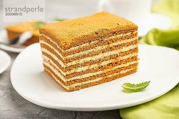 Hausgemachter Honigkuchen mit Milchcreme und Minze mit einer Tasse Kaffee auf einem grauen Betonhintergrund und grünem Textil. Seitenansicht  Nahaufnahme  selektiver Fokus