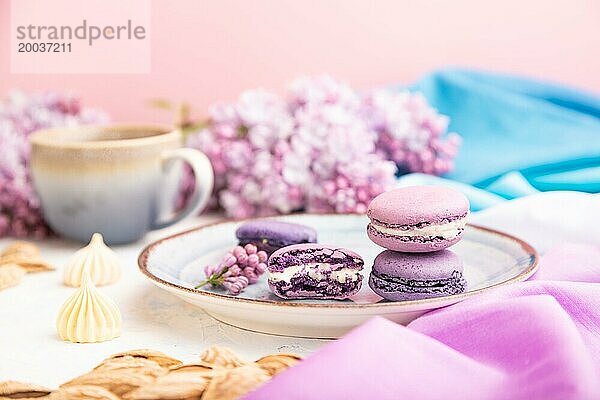 Lila Makronen oder Makronen Kuchen mit Tasse Kaffee auf einem weißen Beton Hintergrund und magenta blaün Textil. Seitenansicht  Nahaufnahme  selektiver Fokus