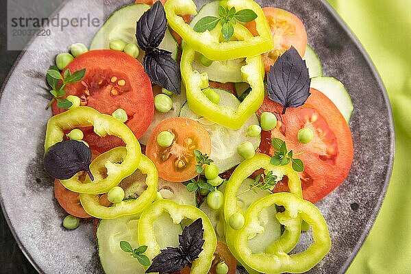 Vegetarischer Salat aus grünen Erbsen  Tomaten  Paprika und Basilikum auf einem grünen Textil. Draufsicht  Nahaufnahme  selektiver Fokus