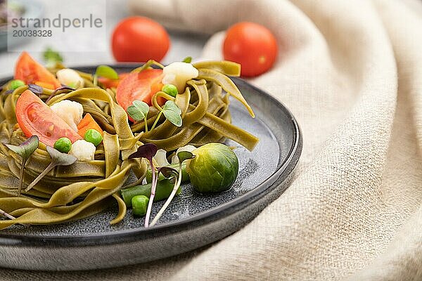 Tagliatelle mit grünem Spinat  Tomaten  Erbsen und Mikrosprossen auf grauem Betonhintergrund und Leinentuch. Seitenansicht  Nahaufnahme  selektiver Fokus