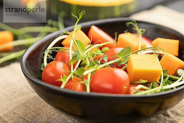 Vegetarischer Gemüsesalat aus Tomaten  Kürbis  mikrogrünen Erbsensprossen auf schwarzem Betonhintergrund und Leinentuch. Seitenansicht  Nahaufnahme  selektiver Fokus