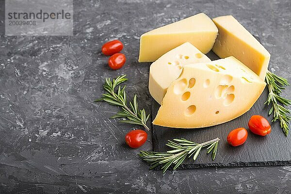 Verschiedene Käsesorten mit Rosmarin und Tomaten auf einer schwarzen Schiefertafel auf einem schwarzen Betonhintergrund. Seitenansicht  Nahaufnahme  Kopierraum  selektiver Fokus