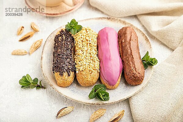 Set von Eclair  traditionelles französisches Dessert und Tasse Kaffee auf grauem Betonhintergrund und Leinenstoff. Seitenansicht  Nahaufnahme  selektiver Fokus  Stillleben. Frühstück  Morgen  Konzept