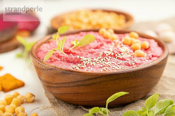 Hummus mit Rüben und mikrogrünen Basilikumsprossen in einer Holzschale auf weißem Holzhintergrund und Leinentuch. Seitenansicht  Nahaufnahme  selektiver Fokus