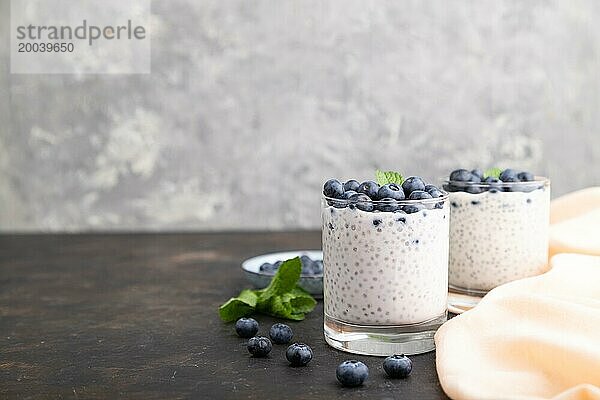 Joghurt mit Heidelbeeren und Chia im Glas auf schwarzem Betonhintergrund und orangefarbenem Leinentextil. Seitenansicht  Kopierraum