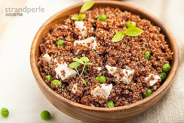 Quinoa Brei mit grünen Erbsen und Huhn in einer Holzschüssel auf einem weißen Holzhintergrund und Leinenstoff. Seitenansicht  Nahaufnahme  selektiver Fokus