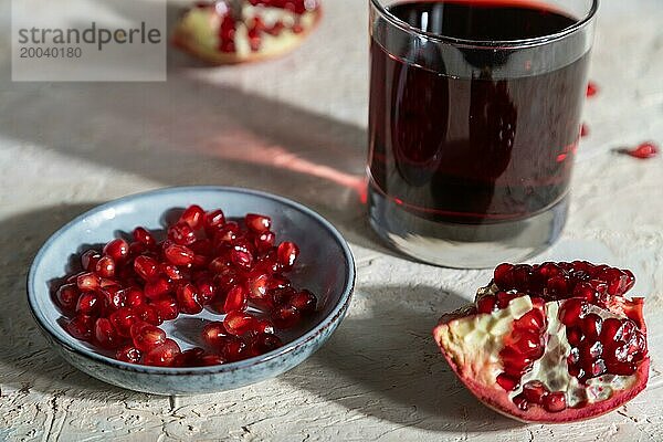 Glas Granatapfelsaft auf einem weißen Betonhintergrund. Hartes Licht  Kontrast. Seitenansicht  Nahaufnahme  selektiver Fokus