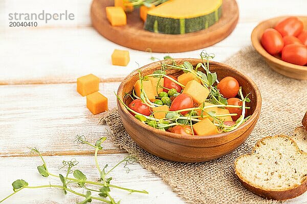 Vegetarischer Gemüsesalat aus Tomaten  Kürbis  mikrogrünen Erbsensprossen auf weißem Holzhintergrund und Leinentuch. Seitenansicht  Nahaufnahme  selektiver Fokus