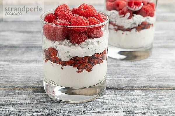 Joghurt mit Himbeeren  Goji Beeren und Chia Samen im Glas auf grauem Holzhintergrund. Seitenansicht  Nahaufnahme  selektiver Fokus