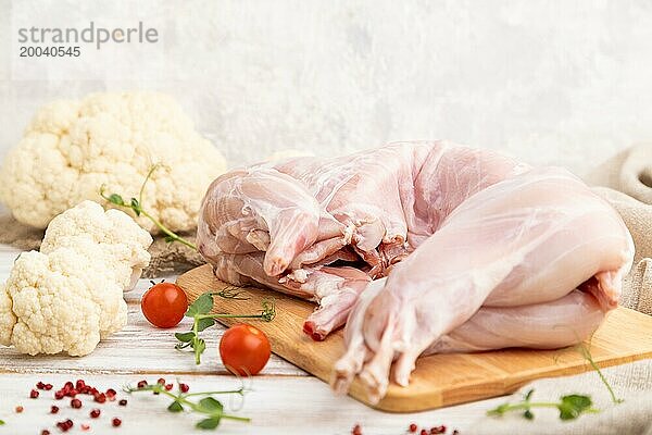 Ganzes rohes Kaninchen mit Blumenkohl  Tomaten und Gewürzen auf einem weißen Holzhintergrund und Leinenstoff. Seitenansicht  Nahaufnahme  selektiver Fokus