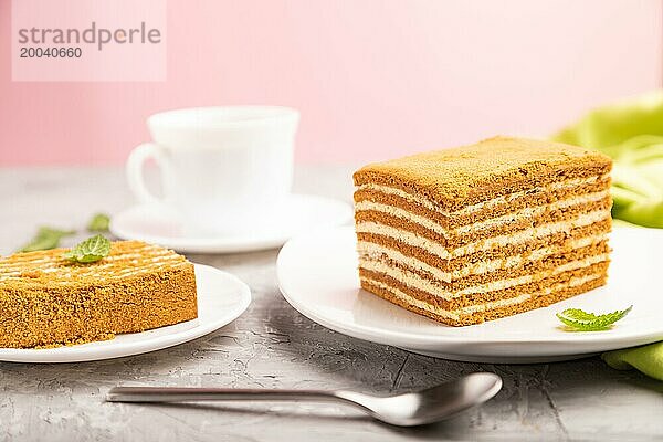 Hausgemachter Honigkuchen mit Milchcreme und Minze mit einer Tasse Kaffee auf einem rosa Hintergrund und grünem Stoff. Seitenansicht  Nahaufnahme  selektiver Fokus