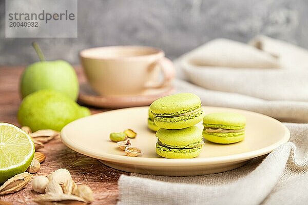 Grüne Macarons oder Makronen Kuchen mit Tasse Kaffee auf einem braunen Beton Hintergrund und Leinen Textil. Seitenansicht  Nahaufnahme  selektiver Fokus