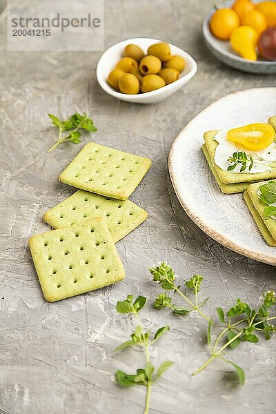 Grüne Cracker Sandwiches mit Frischkäse und Kirschtomaten auf grauem Betonhintergrund. Seitenansicht  Nahaufnahme  selektiver Fokus