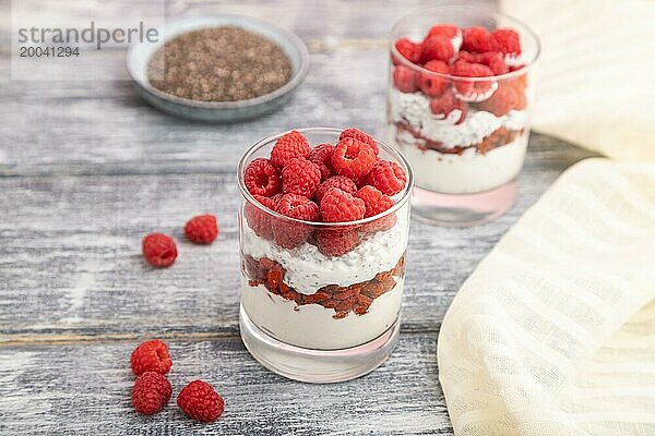 Joghurt mit Himbeeren  Goji Beeren und Chia Samen im Glas auf grauem Holzhintergrund und Leinenstoff. Seitenansicht  Nahaufnahme  selektiver Fokus