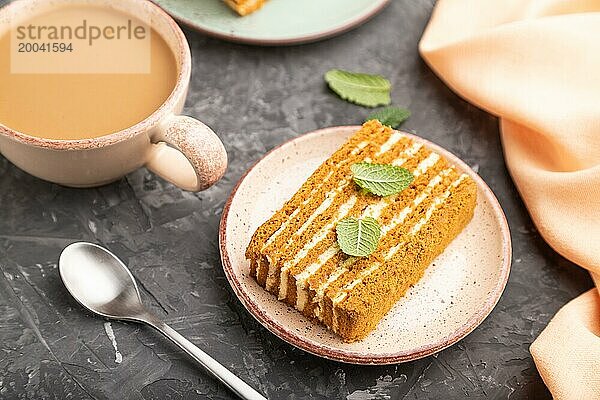 Hausgemachter Honigkuchen mit Milchcreme und Minze mit einer Tasse Kaffee auf einem schwarzen Betonhintergrund und orangefarbenem Textil. Seitenansicht  Nahaufnahme  selektiver Fokus