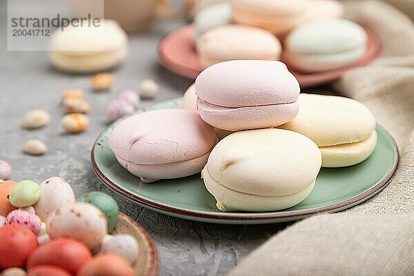 Farbiger Zephir oder Marshmallow mit Kaffeetasse und Dragees auf grauem Betonhintergrund und Leinenstoff. Seitenansicht  Nahaufnahme  selektiver Fokus