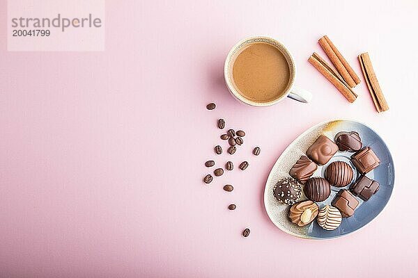 Verschiedene Schokoladenbonbons und eine Tasse Kaffee auf einem rosafarbenen pastellfarbenen Hintergrund. Draufsicht  Flat Lay  Kopierbereich