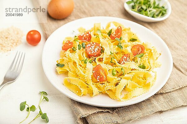 Reginelle Grießnudeln mit Tomaten  Eiern  Sesam und mikrogrünen Sprossen auf weißem Holzuntergrund und Leinenstoff. Seitenansicht  Nahaufnahme  selektiver Fokus