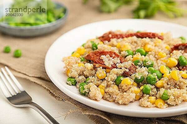 Quinoa Brei mit grünen Erbsen  Mais und getrockneten Tomaten auf einem Keramikteller auf weißem Holzhintergrund und Leinentuch. Seitenansicht  Nahaufnahme  selektiver Fokus