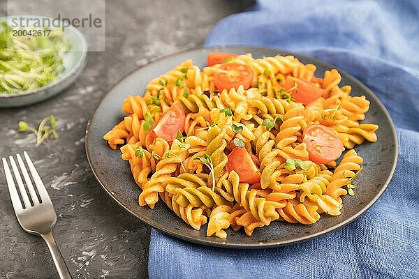 Tortiglioni Grießnudeln mit Tomaten und Mikrogrünsprossen auf einem schwarzen Betonhintergrund und blauem Textil. Seitenansicht  Nahaufnahme  selektiver Fokus