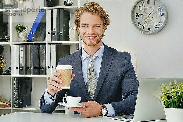 K generiert  Erfolgreicher Jungunternehmer sitzt zufrieden im Büro  30  35  Jahre  Mann  lächelt zufrieden  Existenzgründer  Firmenchef  trinkt einen Becher Kaffee