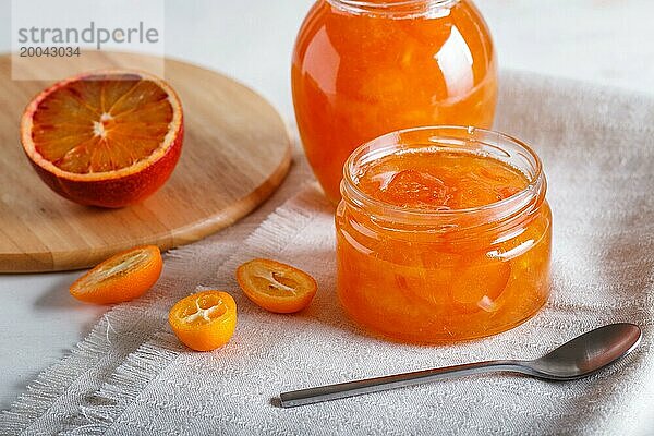 Orangen und Kumquatmarmelade in einem Glas mit frischen Früchten auf einer weißen Leinentischdecke. Hausgemacht  Nahaufnahme