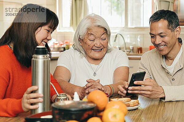 Erwachsene Kinder bringen ihrer älteren Mutter japanischer Herkunft bei  wie man ein Handy benutzt  während sie in der Küche sitzen und Mate trinken. Argentinisch japanische Familie