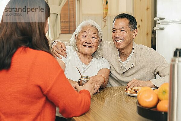 Glückliche erwachsene Kinder  die gemeinsam mit ihrer älteren japanischen Mutter in der Küche Mate trinken. Argentinisch japanische Familie