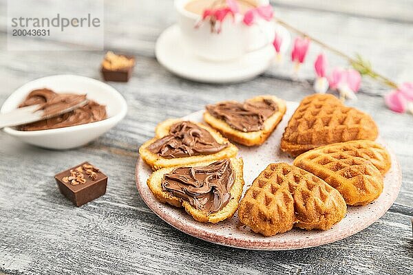 Hausgemachte Waffel mit Schokoladenbutter und Tasse Kaffee auf einem grauen Holzhintergrund. Seitenansicht  selektiver Fokus  Nahaufnahme