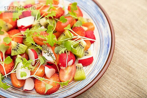 Vegetarischer Obst und Gemüsesalat aus Erdbeeren  Kiwi  Tomaten  Mikrogrünsprossen auf schwarzem Betonhintergrund und Leinentextil. Seitenansicht  Nahaufnahme  selektiver Fokus