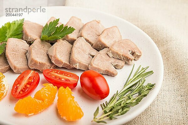 Gekochte Schweinezunge mit Tomaten und Kräutern auf einem grauen Betonhintergrund und Leinenstoff. Seitenansicht  Nahaufnahme  selektiver Fokus