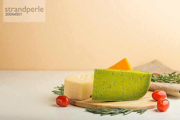 Grüner Basilikumkäse und verschiedene Käsesorten mit Rosmarin und Tomaten auf einem Holzbrett auf einem weißen Holzhintergrund. Seitenansicht  Kopierraum  selektiver Fokus